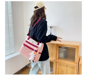 Detailed view of a pink and white canvas tote bag with shoulder strap and duck plush charm