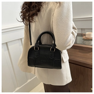 Detail of matte black handbag with QRN logo and gold hardware worn on a tweed jacket