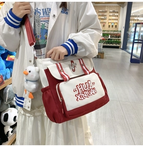 Detail of red and white canvas messenger bag with a cute plush duck charm in lifestyle setting