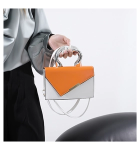 Close-up of modern orange and white contrast square bag with unique silver metal handle