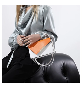 Detail of orange and white leather bag with geometric fold and silver metal ring handle
