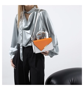 Artistic silver metal handle on a color-block crossbody bag with bright orange V-flap