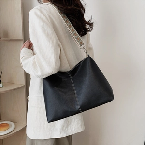 Large black leather tote bag with wide geometric strap shown on model in a cozy room