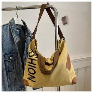Détail du sac cabas en toile jaune avec imprimé FASHION sur un cintre près d'un jean