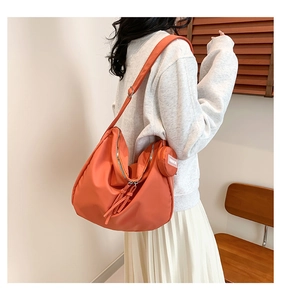 Détail d'un sac bandoulière orange en nylon avec une petite pochette ronde assortie attachée