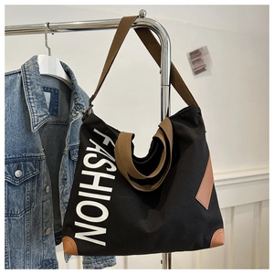 Détail d'un grand sac cabas en toile noire suspendu à côté d'une veste en jean bleue