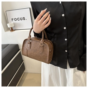 Detail view of deep brown Boston handbag with embossed ORNI logo and leather texture