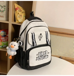Detail of black and white student backpack featuring cute duck pendant and art lettering