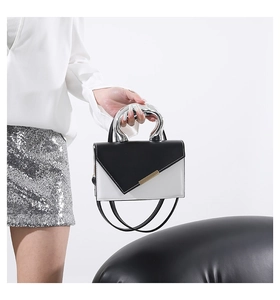 Detail of contrast handbag with silver metal circular handle and geometric flap design