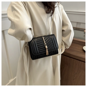 Détail d'un sac bandoulière noir avec matelassage en V et pompon doré sur modèle