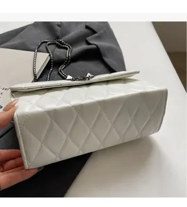 Detail view of white quilted faux leather texture and metallic chain on a crossbody bag