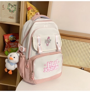 Pink and white canvas backpack with a cute duck charm on a wooden shelf setting
