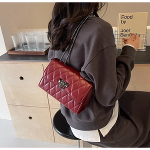 Close-up of wine red quilted chain bag with studded metal clasp worn by a model