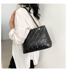 Détail du sac fourre-tout noir matelassé avec chaîne dorée et coutures géométriques