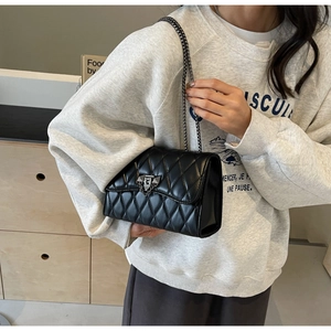 Detail of black quilted leather shoulder bag with vintage metal lock and chain strap