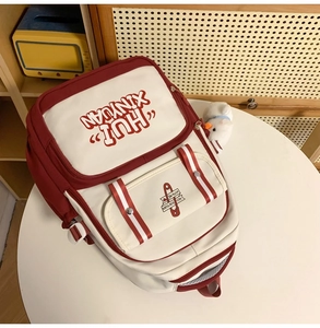 Detail of red and white backpack with plush duck charm and HUI XIN YUAN lettering