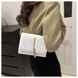 Détail d'un sac bandoulière blanc matelassé avec chaîne dorée et décoration de gland