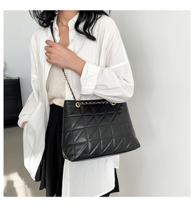Détail d'un sac cabas noir matelassé avec chaîne dorée porté par un mannequin femme