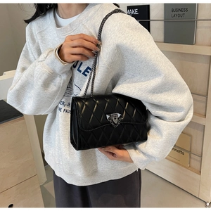 Detail showing the black quilted pattern texture and dark grey metal chain of the shoulder bag