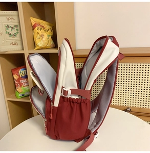 Detail of red and white backpack showing multiple zippered compartments and breathable straps