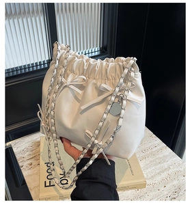 Détail d'un sac seau en cuir blanc avec bandoulière chaîne et nœud décoratif