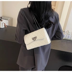 Close-up of a white quilted crossbody bag with a dark grey metal lock and chain strap