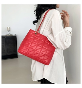 Détail du sac cabas rouge matelassé avec bandoulière en chaîne dorée et finition brillante