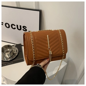 Détail du sac à bandoulière matelassé marron avec chaîne dorée et pompon décoratif