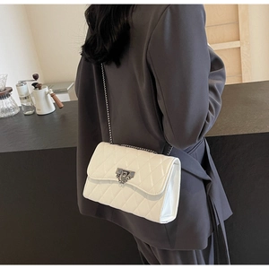 Close-up of white quilted leather shoulder bag featuring silver chain and metal buckle