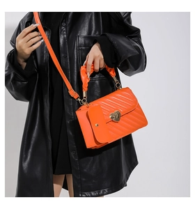 Detail of orange faux leather crossbody bag with heart lock and ruched handle shown on model