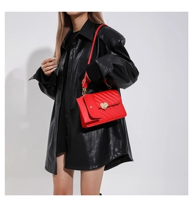 Detailed close-up of red quilted handbag with golden heart-shaped metal buckle and V-stitch pattern