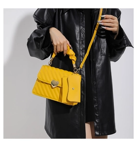 Detail of yellow quilted handbag featuring heart buckle and pleated handle on a black shirt