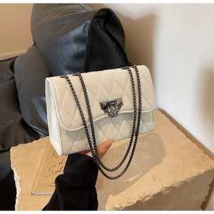 Close-up of quilted white crossbody bag featuring dark metal chain and secure flip-lock buckle