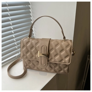 Detail of beige quilted faux leather handbag showing golden metal clasp and handle texture