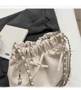 Détail d'un sac seau blanc crème avec bandoulière en chaîne et décoration en nœud