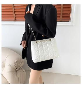 Sac bandoulière matelassé blanc avec chaîne dorée porté sur un blazer noir élégant