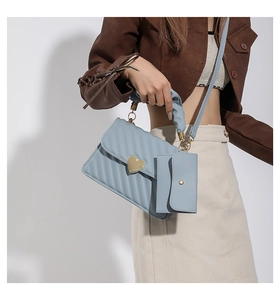 Detail of light blue crossbody bag with gold heart lock and elegant V-shaped quilting
