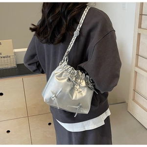 Détail d'un sac seau argenté métallisé avec nœuds et bandoulière chaîne porté par un mannequin