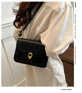 Detail of a black leather crossbody bag with a gold double ring buckle and shoulder strap