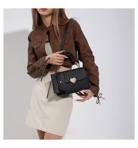 Close-up of black quilted handbag with gold heart clasp and pleated handle detail
