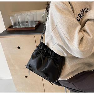 Détail du sac seau noir avec nœuds décoratifs et bandoulière chaîne en cuir