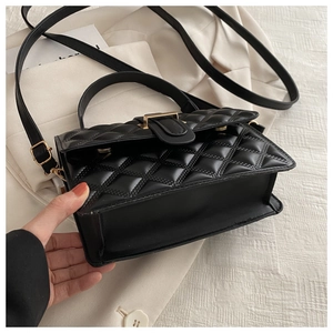 Close-up of black quilted PU leather bag with golden square lock and leather strap
