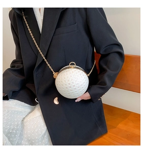 Close-up of white spherical clutch with pearl texture and gold chain worn by a model