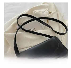 Close-up of black leather crossbody bag with golden metal buckle and stitching detail