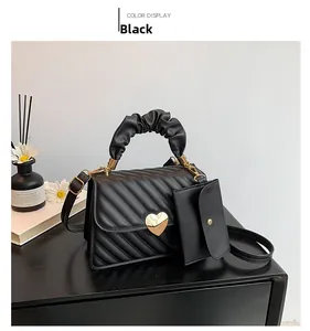 Detail of black quilted crossbody bag featuring gold heart lock and ruffled cloud handle