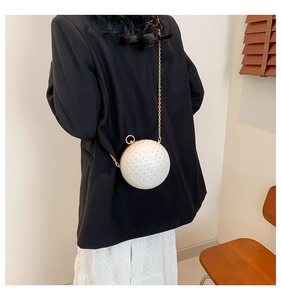 Detail of elegant round pearl evening bag with gold metal chain on a black suit