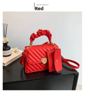 Detail of red quilted handbag with gold heart buckle and pleated handle on dark wood surface