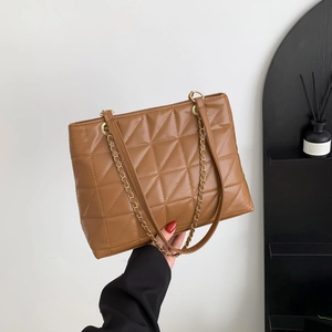 Sac fourre-tout matelassé marron avec chaîne dorée tenu par une personne en blazer