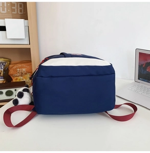 Detail of color block nylon backpack in navy and white with red straps and panda pendant