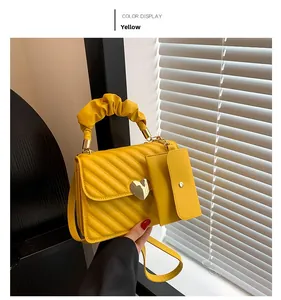 Detail of yellow quilted handbag featuring a ruffled handle and heart-shaped buckle